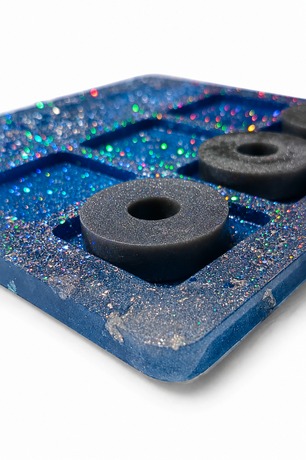 Dettaglio ravvicinato del tris in resina argento e blu glitter con pedine, spessore della base e riflessi olografici