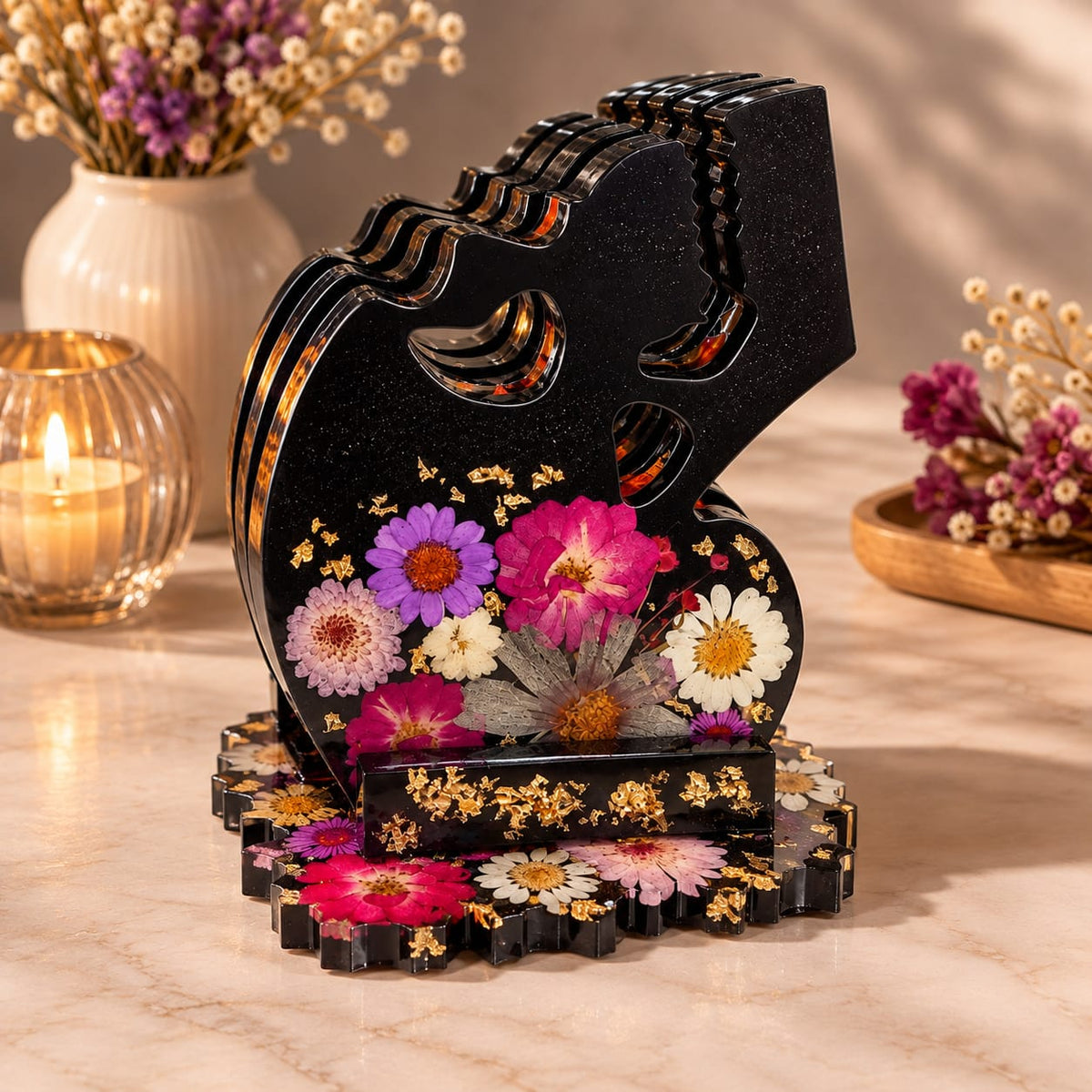 Sottobicchieri a forma di teschio con fiori pressati, sistemati nel supporto artigianale in resina nera, decorato con fiori e sfoglia oro.