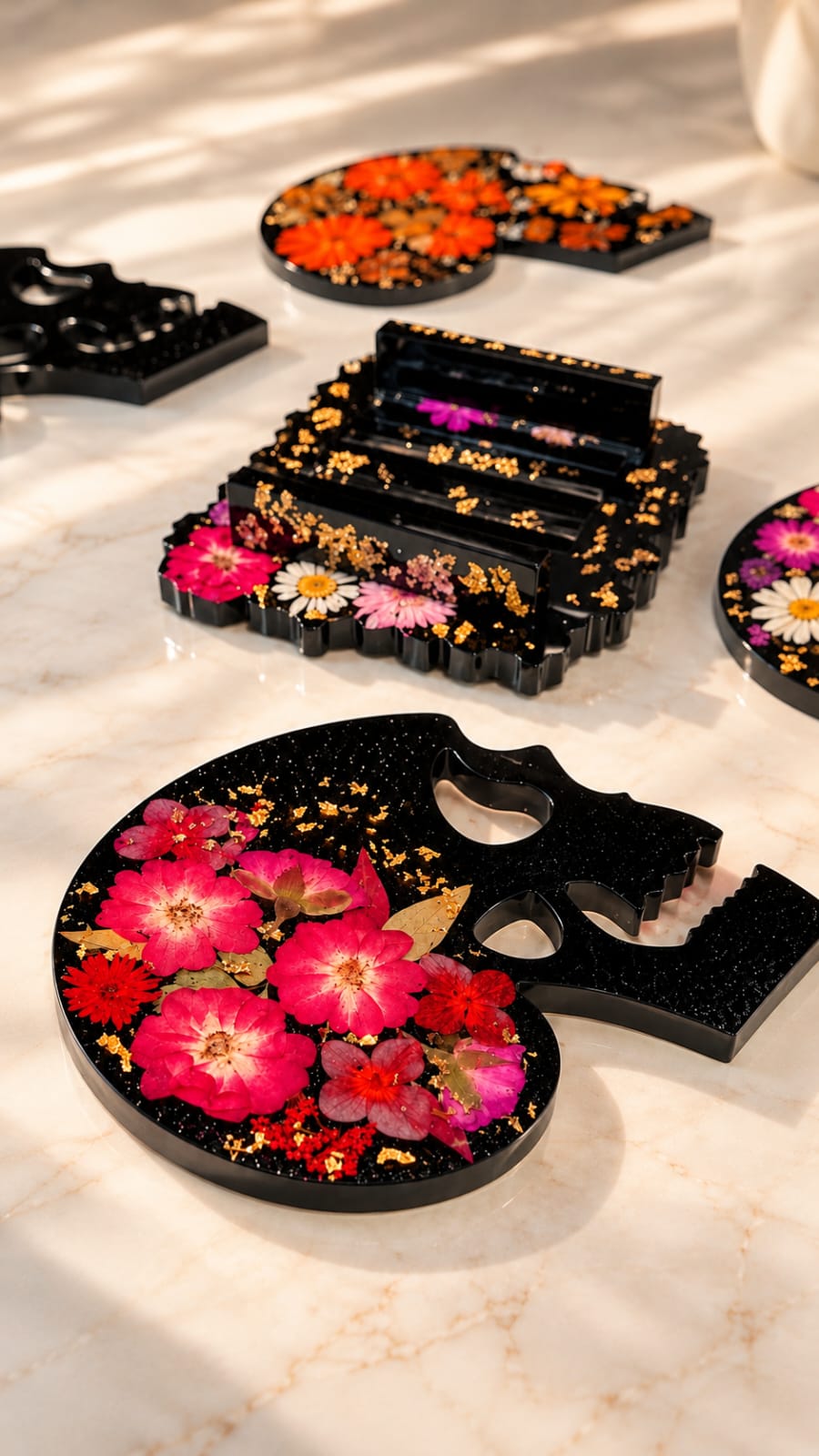 Dettaglio dei sottobicchieri a forma di teschio realizzati in resina, con fiori pressati colorati racchiusi nella trasparenza del materiale e fondo nero.