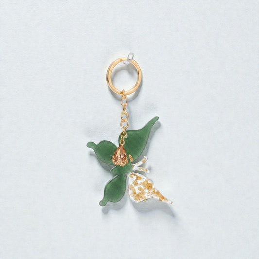 Aurea portachiavi farfalla artigianale in resina verde con foglia d'oro e cristallo champagne su sfondo bianco
