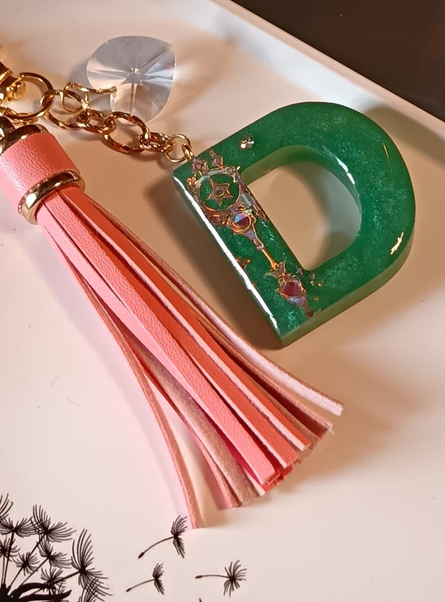 Primo piano ciondolo portachiavi lettera D in resina con charm e nappina pelle sintetica, pezzo unico