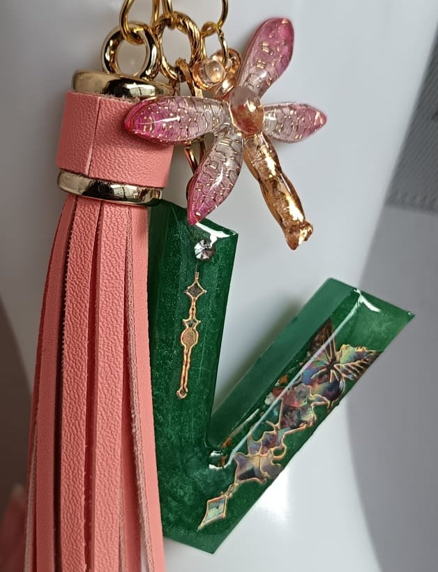 Primo piano ciondolo lettera V personalizzata in resina con charm e nappina corallo pelle sintetica, pezzo unico